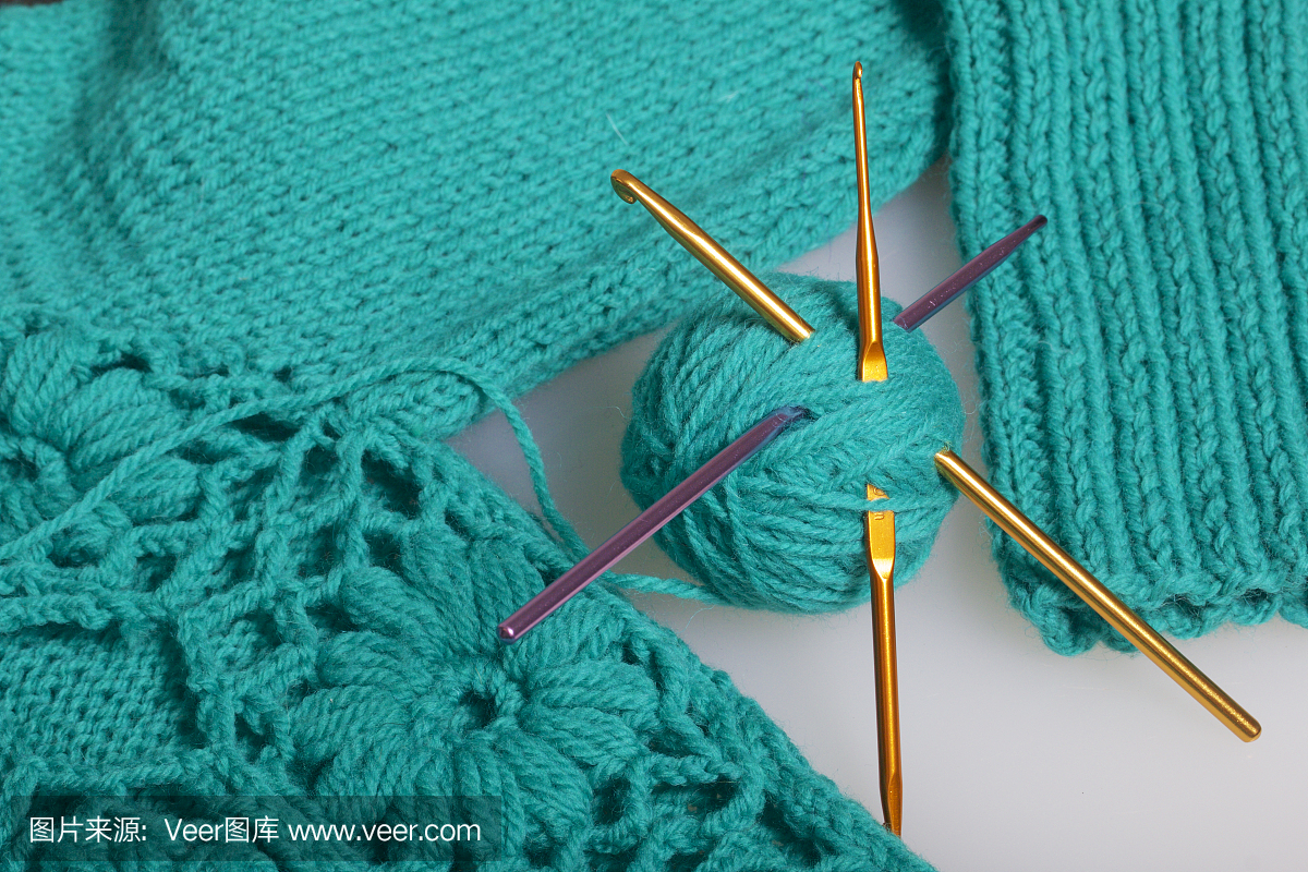 翠绿色编织用线串和编织用钩。躺在现成的针织产品上。
